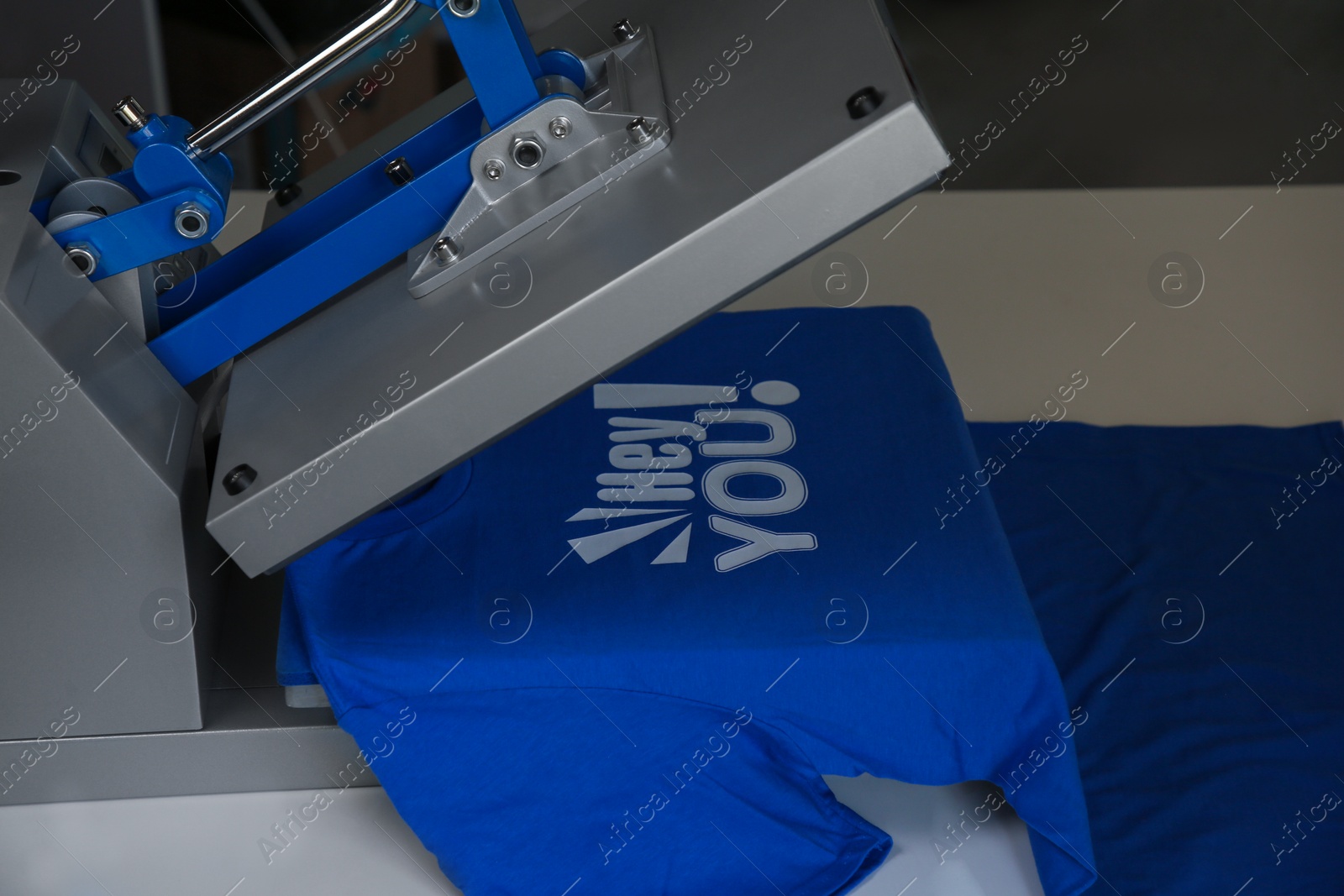 Photo of Printing logo. Heat press with blue t-shirt on white table