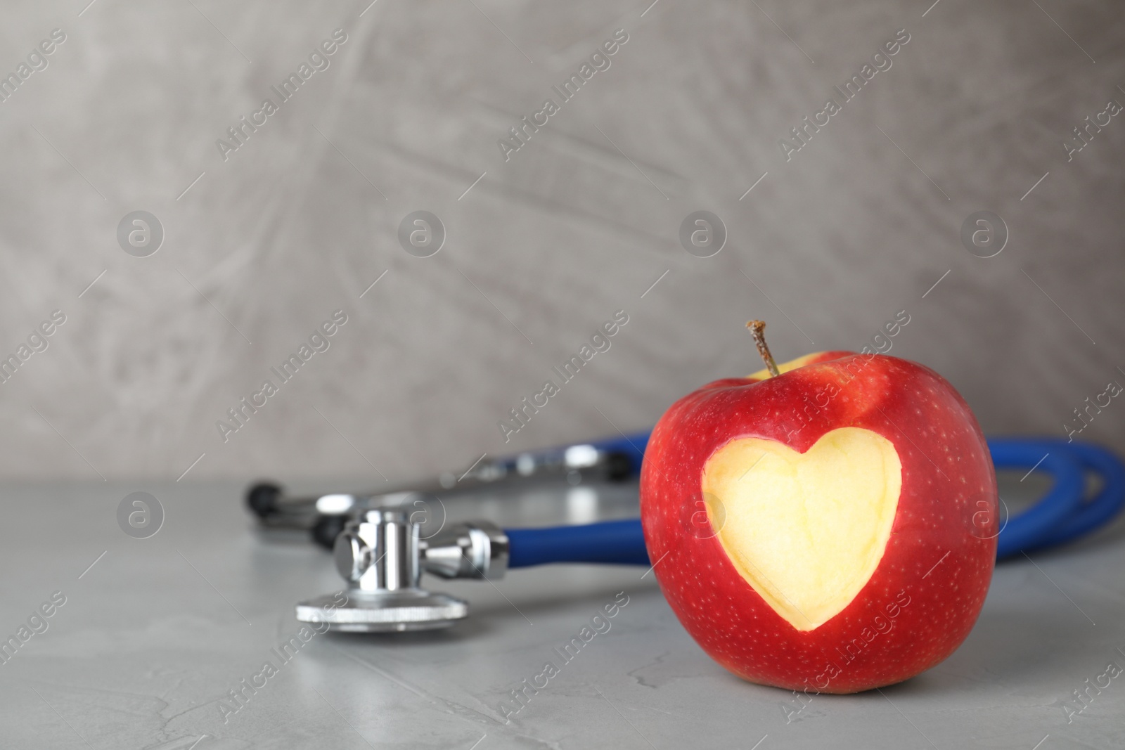 Photo of Red apple with carved heart and stethoscope on table. Space for text