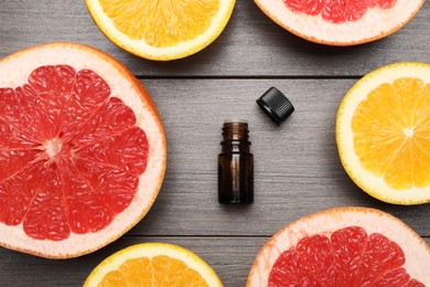 Bottle of citrus essential oil and fresh fruits on wooden table, flat lay