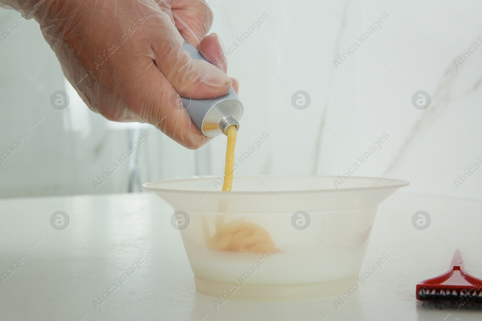 Photo of Woman preparing hair dye in bowl at white table, closeup