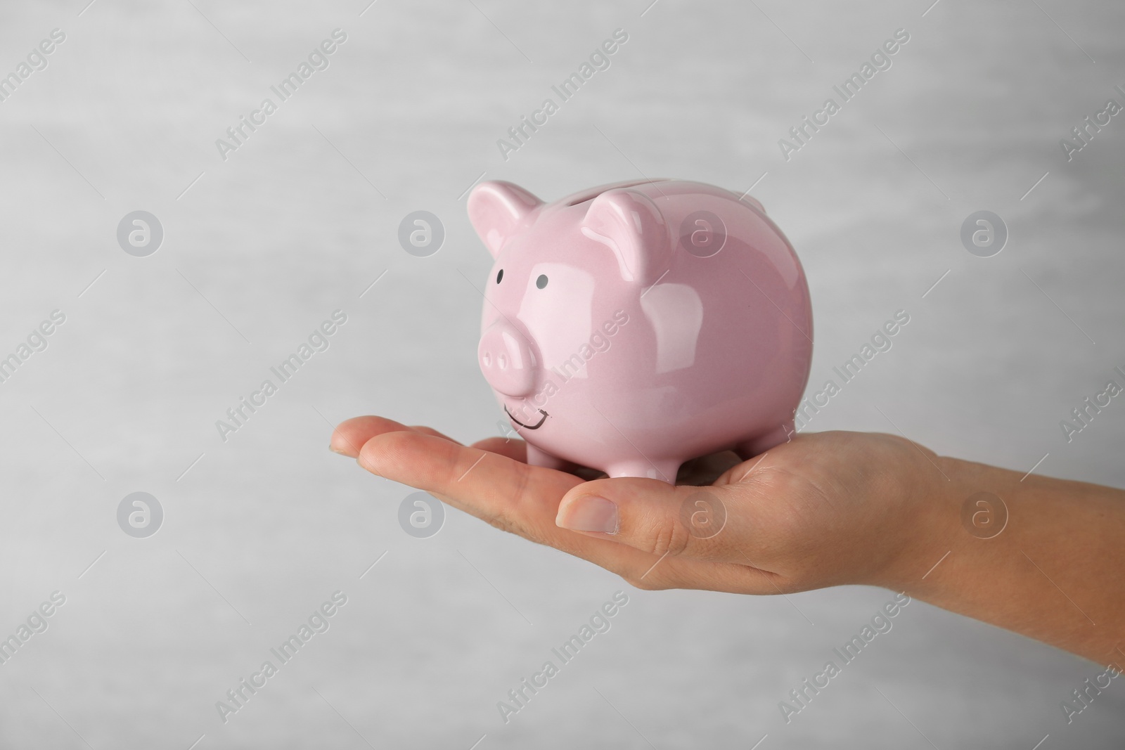Photo of Woman holding piggy bank on grey background, closeup view
