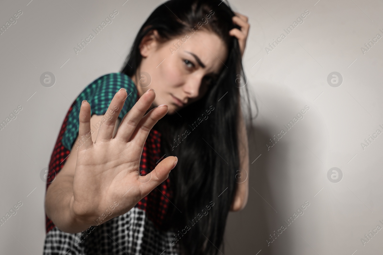 Photo of Young woman making stop gesture against light background, focus on hand