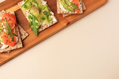 Photo of Fresh crunchy crispbreads with cream cheese, cucumber, green onion, salmon and arugula on beige table, top view. Space for text