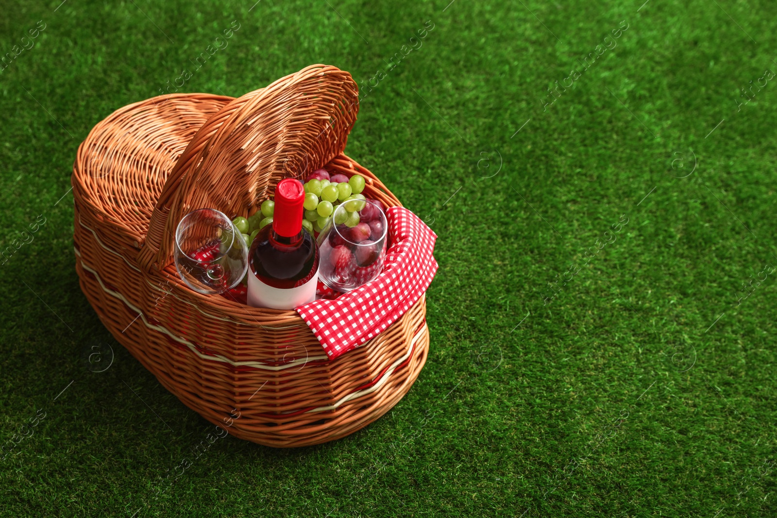 Photo of Picnic basket with wine and grapes on grass, space for text