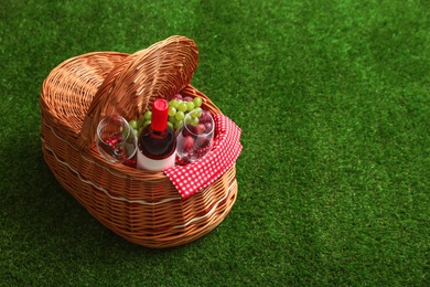 Picnic basket with wine and grapes on grass, space for text