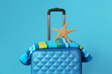 Stylish suitcase with towel and sea star on color background