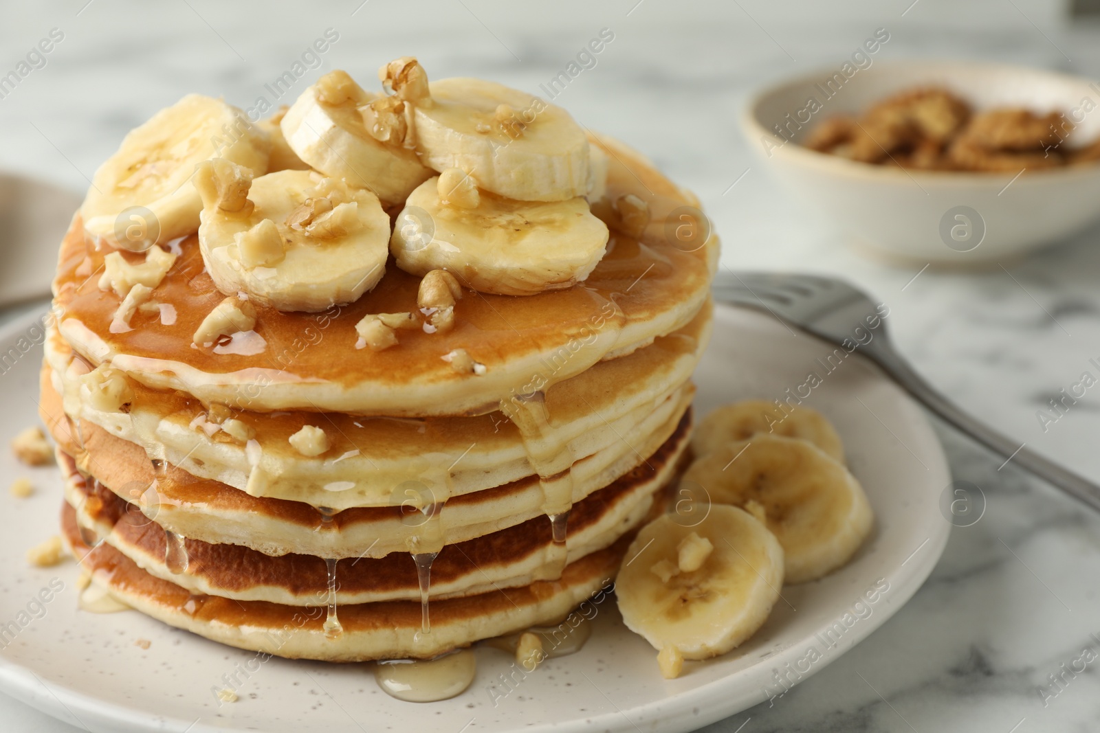 Photo of Delicious pancakes with bananas, walnuts and honey on white marble table, closeup