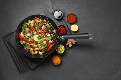 Photo of Stir-fry. Tasty noodles with meat in wok, chopsticks and ingredients on grey textured table, flat lay