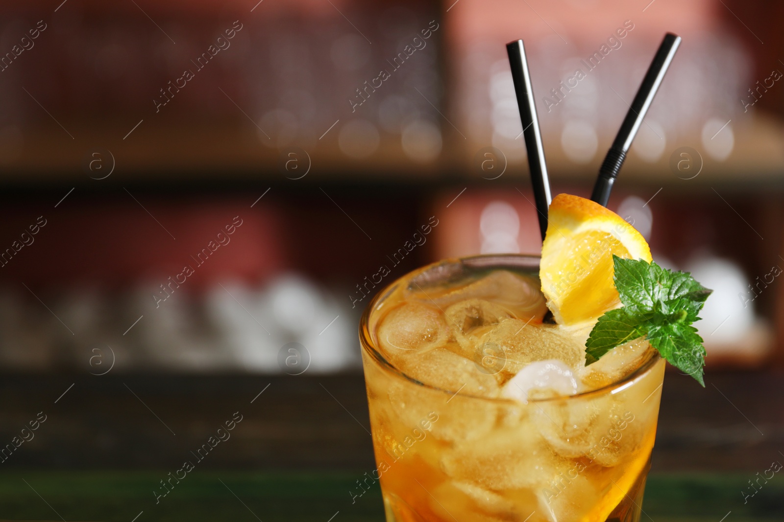 Photo of Glass of delicious cocktail with ice on blurred background, closeup