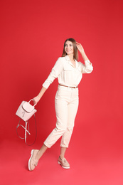 Beautiful young woman in casual outfit with stylish bag on red background