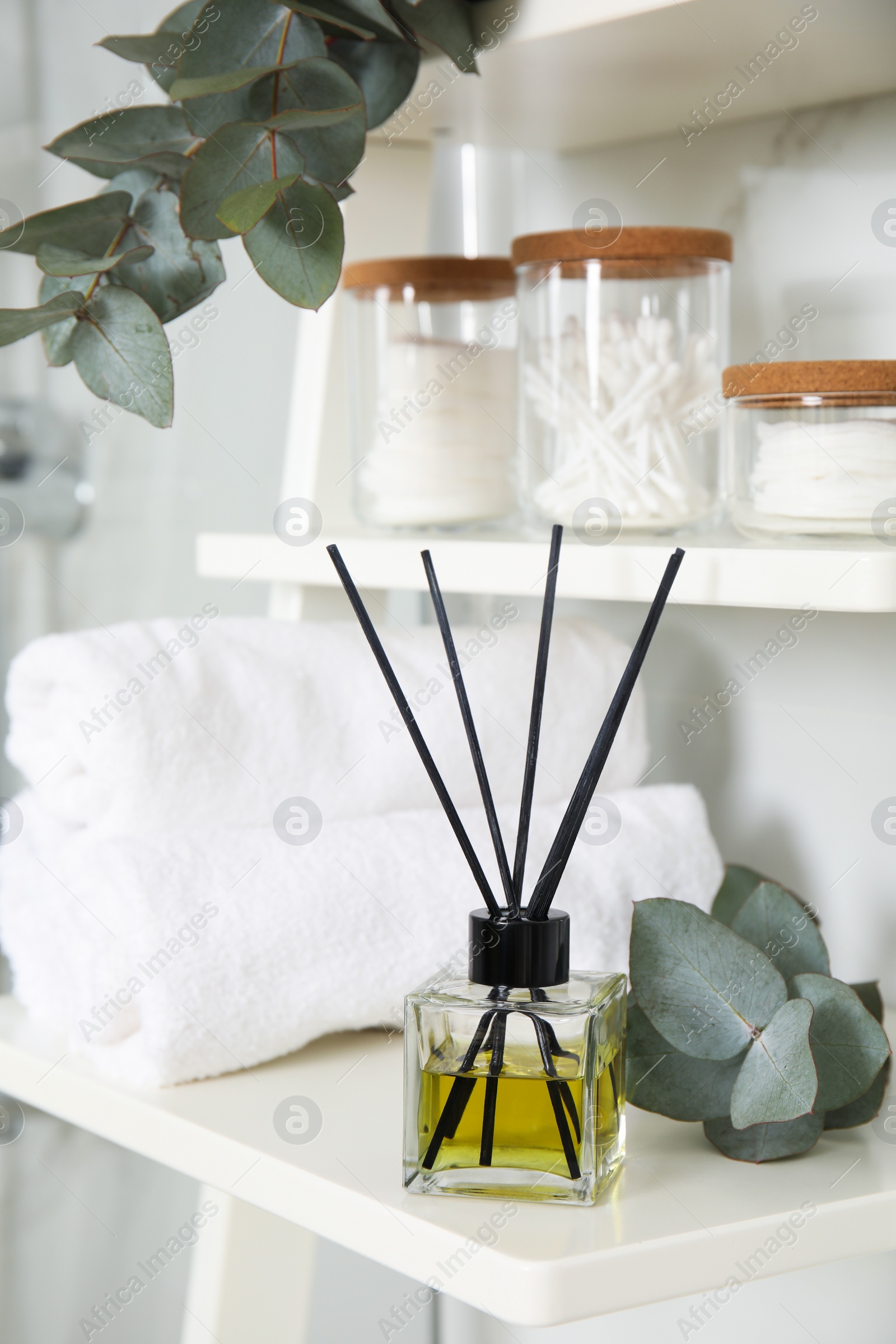 Photo of Aromatic reed air freshener, toiletries and rolled towels on white wooden shelf in bathroom