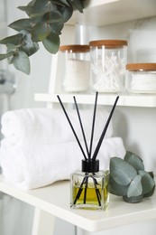 Aromatic reed air freshener, toiletries and rolled towels on white wooden shelf in bathroom