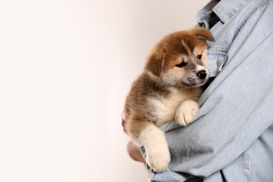 Photo of Woman holding Akita Inu puppy on light background, closeup. Space for text