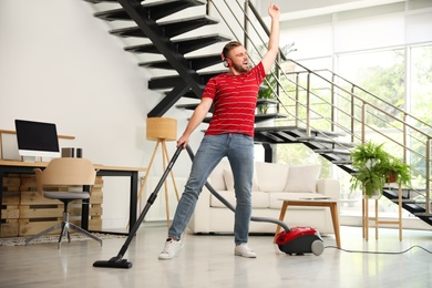 Photo of Young man having fun while vacuuming in living room