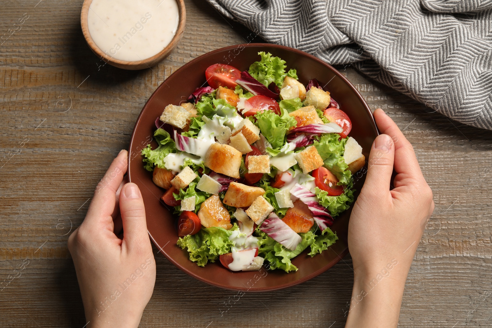 Photo of Woman with plate of delicious Caesar salad at wooden table, top view