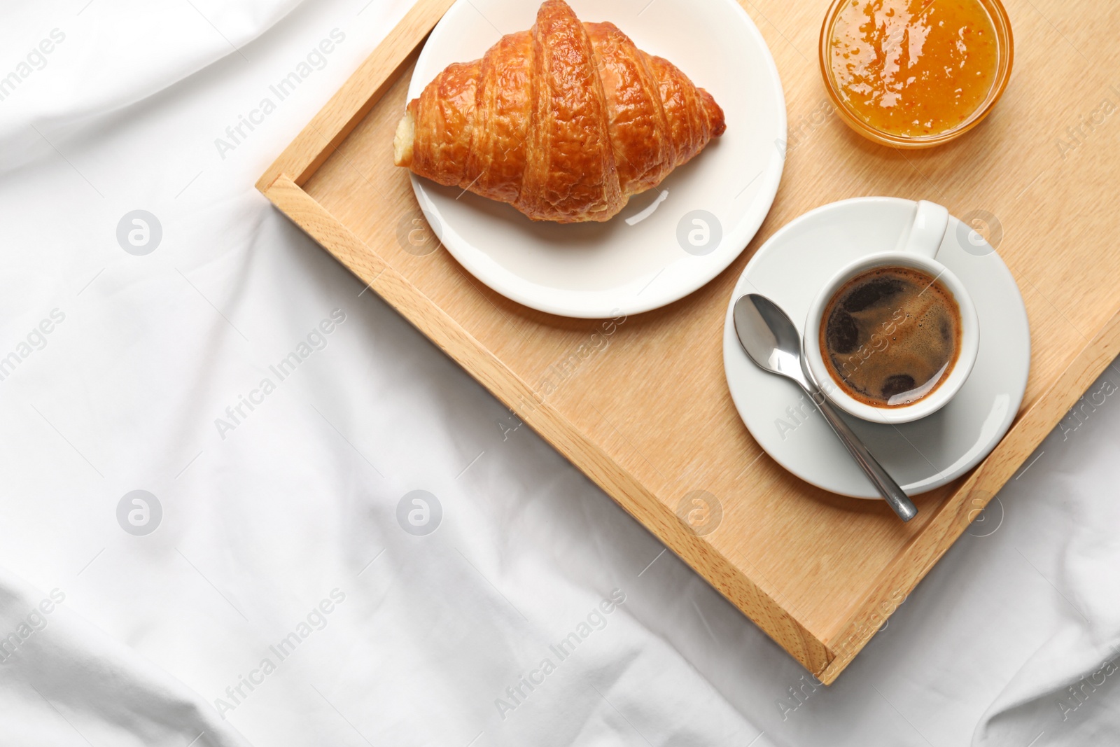 Photo of Top view of wooden tray with coffee, croissant and jam on white fabric, space for text. Breakfast in bed