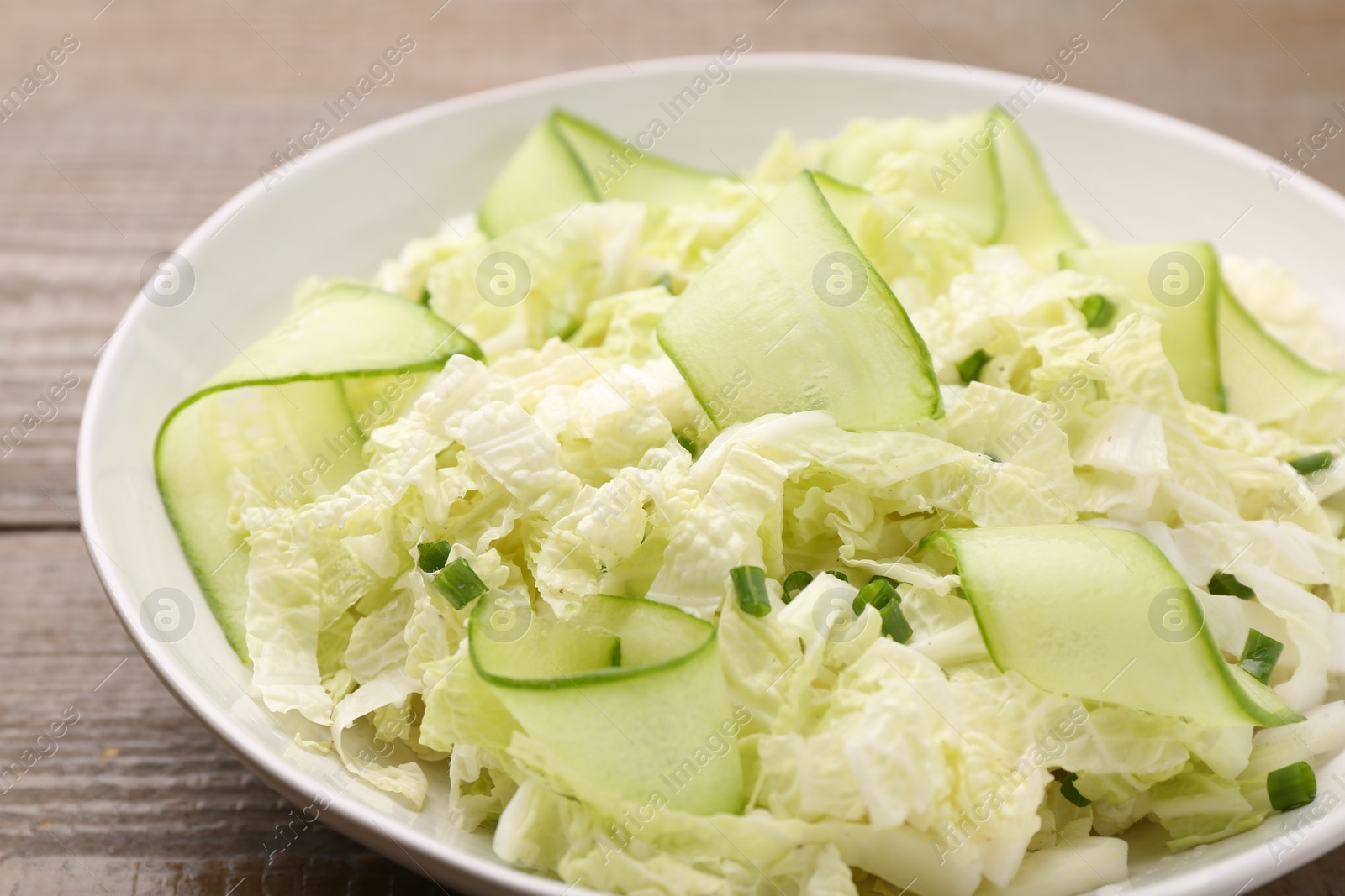 Photo of Tasty salad with Chinese cabbage, cucumber and green onion in bowl on wooden table, closeup