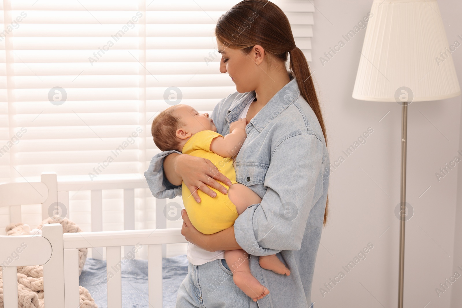 Photo of Mother holding her sleeping newborn baby in child's room