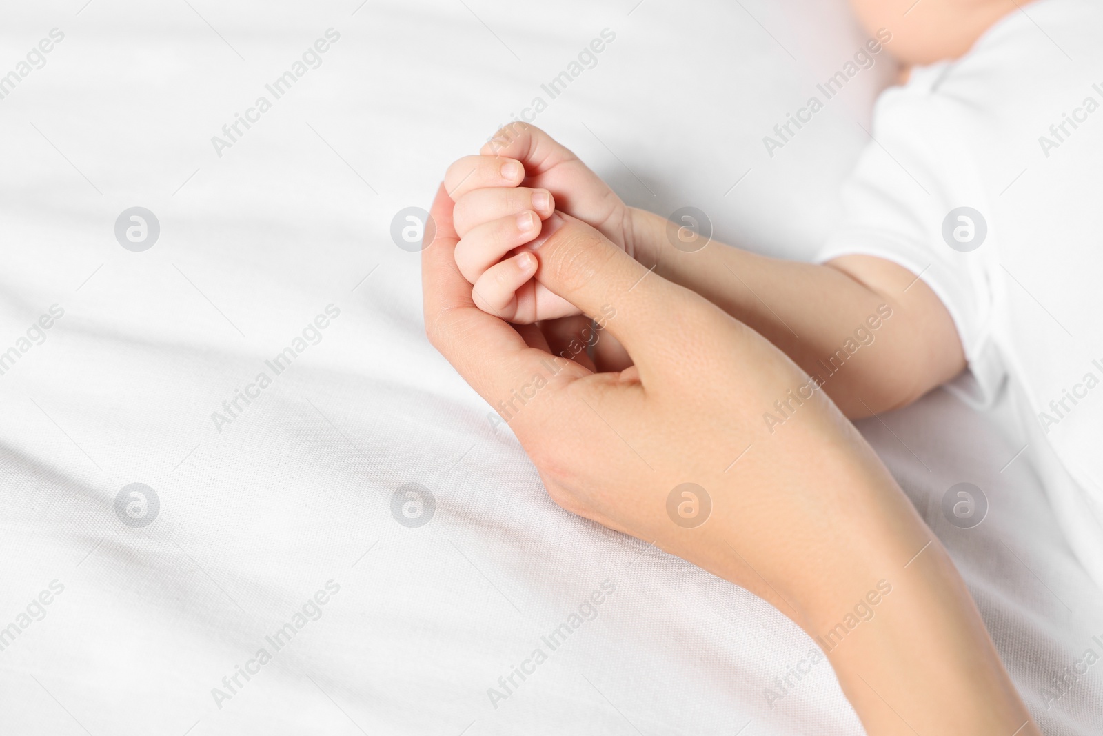 Photo of Mother holding hand of her little baby on bed, closeup