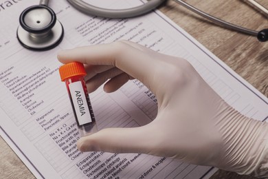 Photo of Doctor holding test tube with blood sample and label Anemia over table, closeup