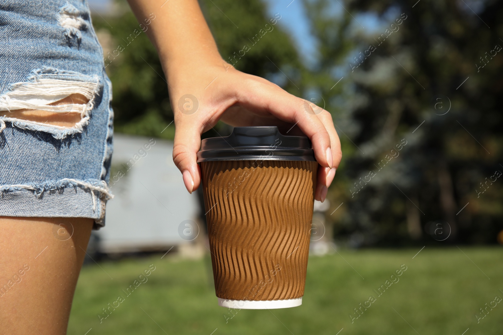 Photo of Woman holding takeaway cardboard coffee cup with plastic lid outdoors, closeup