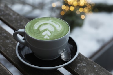 Photo of Cup of fresh matcha latte on wooden bench outdoors in winter, closeup
