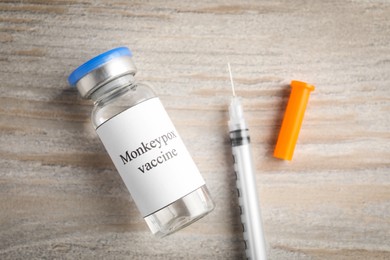 Photo of Monkeypox vaccine in glass vial and syringe on wooden table, flat lay