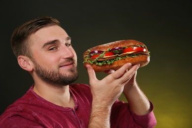 Young hungry man with tasty burger on color background