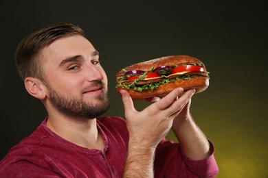 Photo of Young hungry man with tasty burger on color background