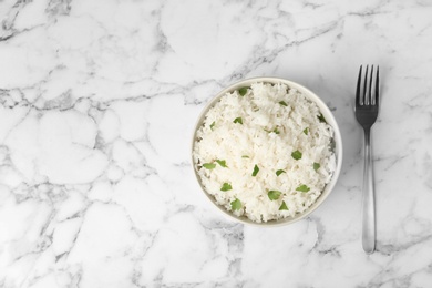 Photo of Bowl of boiled rice and fork on marble background, top view with space for text