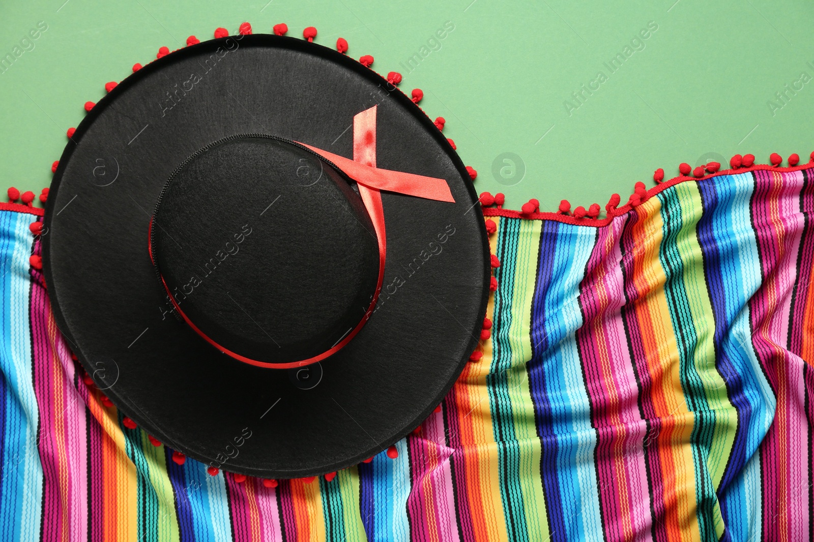 Photo of Mexican sombrero hat and colorful poncho on green background, flat lay
