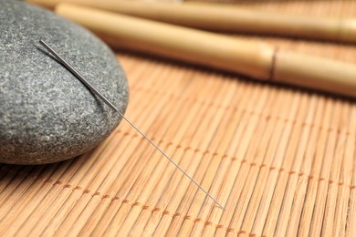 Photo of Acupuncture needle and spa stone on bamboo mat, closeup. Space for text