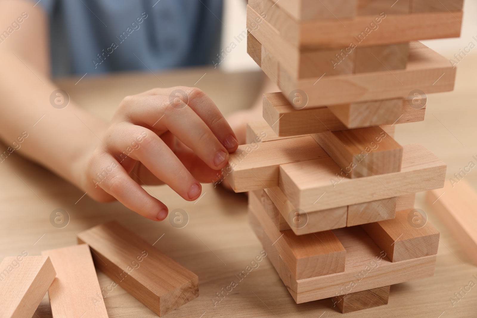 Photo of Child playing Jenga at wooden table indoors, closeup