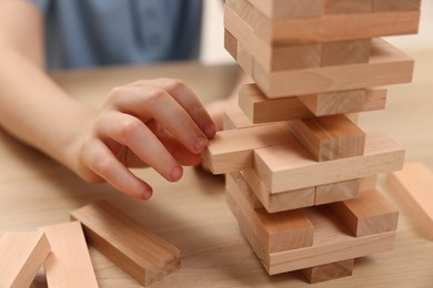 Photo of Child playing Jenga at wooden table indoors, closeup