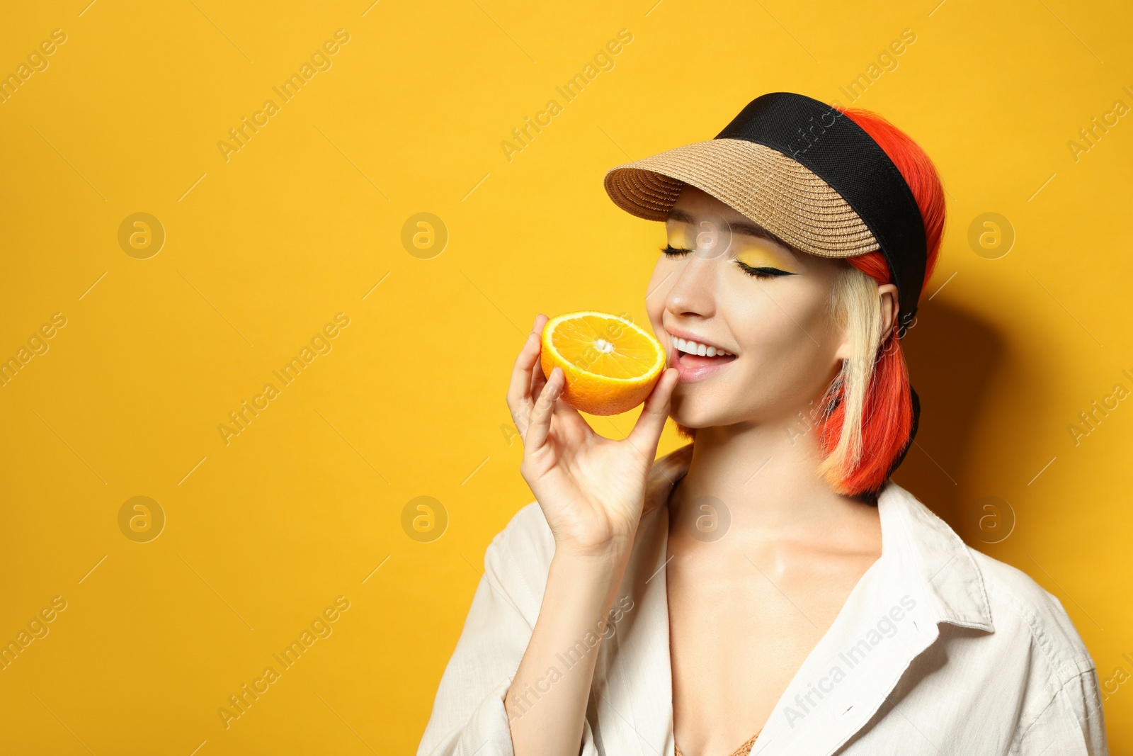 Photo of Beautiful young woman with bright dyed hair eating orange on color background, space for text