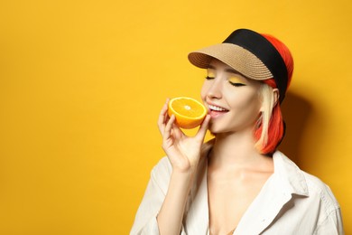 Beautiful young woman with bright dyed hair eating orange on color background, space for text