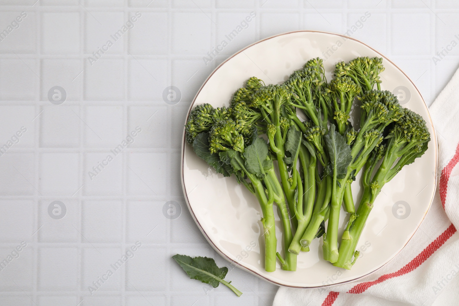 Photo of Fresh raw broccolini on white tiled table, top view and space for text. Healthy food