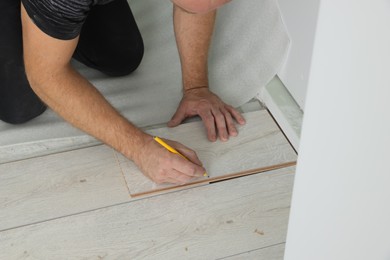 Photo of Man using pencil during installation of new laminate flooring, closeup