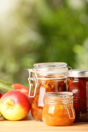 Photo of Delicious apple jams and fresh fruits on wooden table