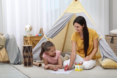 Photo of Mother and daughter drawing near toy wigwam at home