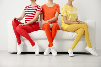 Women wearing bright tights sitting on sofa indoors, closeup