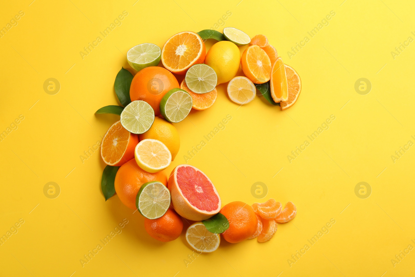 Photo of Letter C made with citrus fruits on yellow background as vitamin representation, flat lay