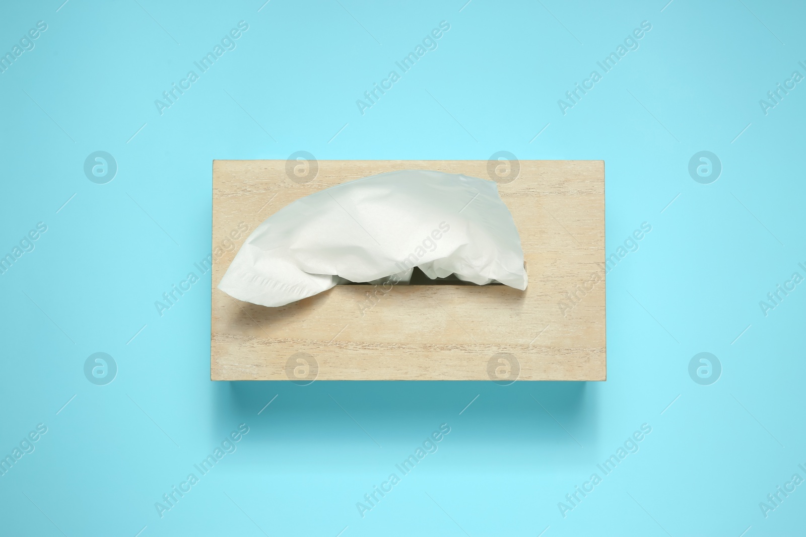 Photo of Wooden holder with paper tissues on light blue background, top view