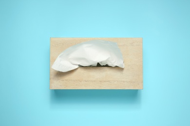 Photo of Wooden holder with paper tissues on light blue background, top view