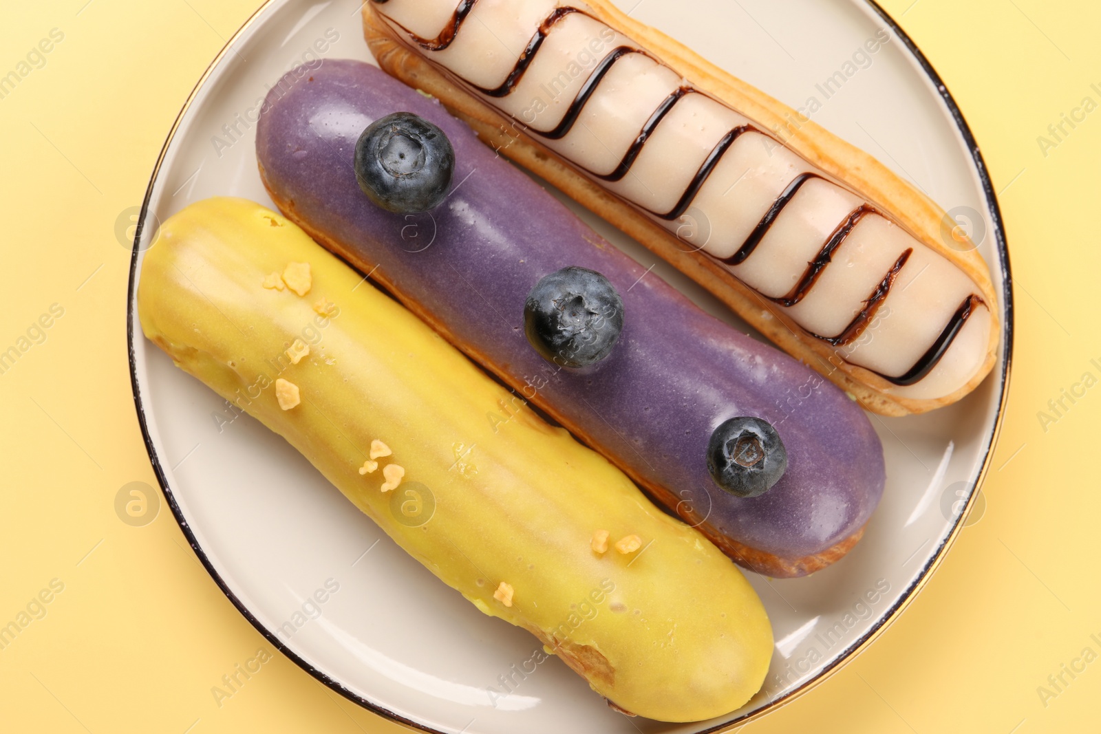 Photo of Delicious eclairs covered with glaze on yellow background, top view