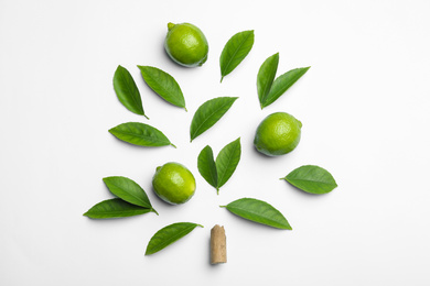 Composition with fresh green citrus leaves and limes on white background, top view