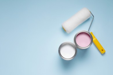 Cans with different paints and roller on light blue background, flat lay. Space for text