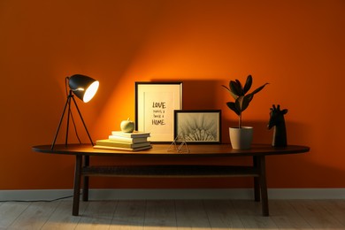 Photo of Wooden coffee table with different decor near orange wall indoors. Stylish interior design