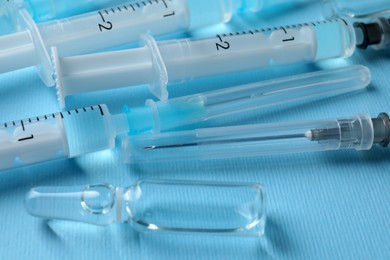 Photo of Disposable syringes with needles and ampule on light blue background, closeup