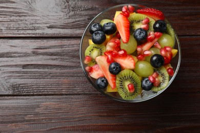 Tasty fruit salad in bowl on wooden table, top view. Space for text